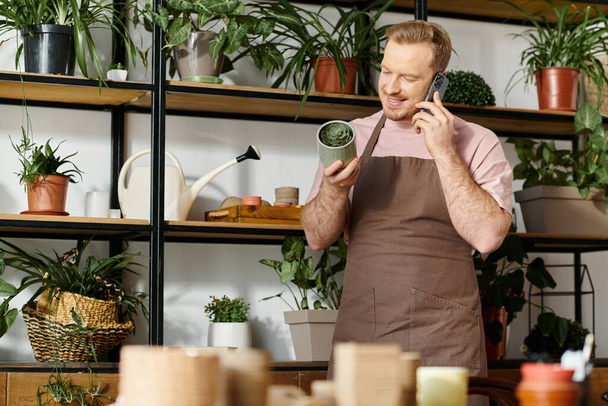 Чоловік у фартусі розмовляє на мобільному телефоні в магазині рослин, втілюючи дух володіння маленьким бізнесом. - Фото, зображення