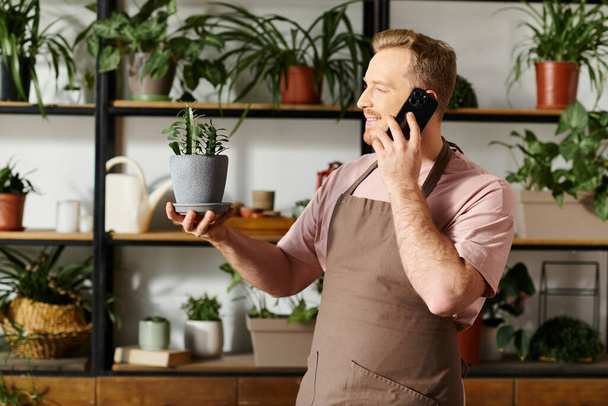 Ein Mann, der Multitasking betreibt, indem er mit einem Handy spricht und eine Topfpflanze in einem Pflanzenladen hält. - Foto, Bild