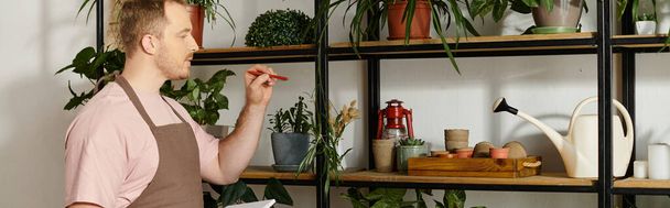 Bello uomo si erge orgogliosamente di fronte a uno scaffale pieno di varie piante in vaso nel suo negozio di piante. - Foto, immagini