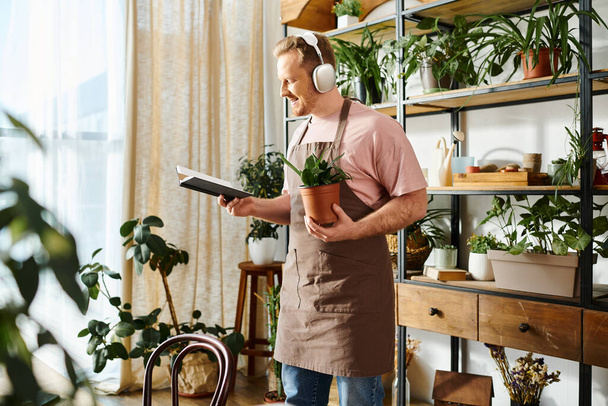 スタイリッシュなエプロンの男は,明るく空気のある植物の店の設定で慎重に植物を保持しています. - 写真・画像