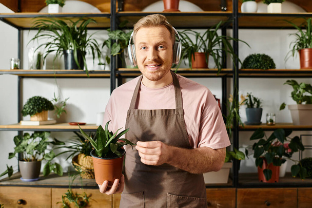 Um homem em um avental prende cuidadosamente uma planta potted, mostrando sua dedicação a seu negócio pequeno do florist. - Foto, Imagem