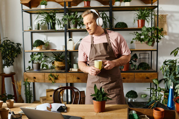 Mężczyzna w fartuchu pijący kawę w sklepie z roślinami, prezentujący koncepcję posiadania małego biznesu.. - Zdjęcie, obraz
