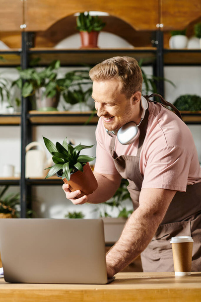 Um homem que ostenta fones de ouvido concentra-se em seu laptop, imerso na gestão de suas operações de lojas de plantas. - Foto, Imagem