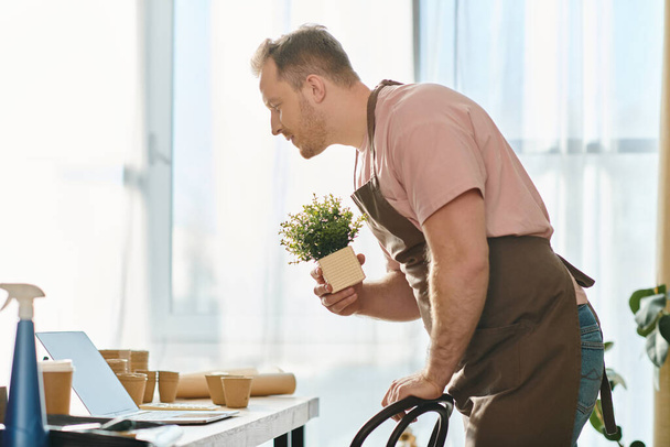 Un uomo tende a una pianta in vaso mentre lavora sul suo computer portatile, simboleggiando la crescita virtuale nel suo business negozio di piante. - Foto, immagini