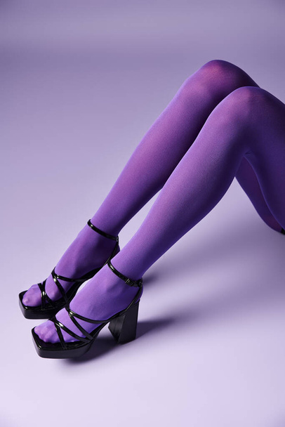 Молодая женщина уверенно стоит на высоких каблуках и ярких фиолетовых чулках на фиолетовом фоне в студии. - Фото, изображение