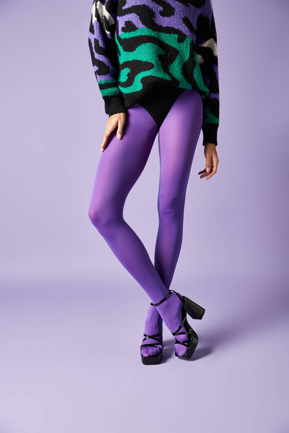 Jonge vrouw gekleed in levendige paarse panty en een trui slaan een pose in een studio tegen een paarse achtergrond. - Foto, afbeelding