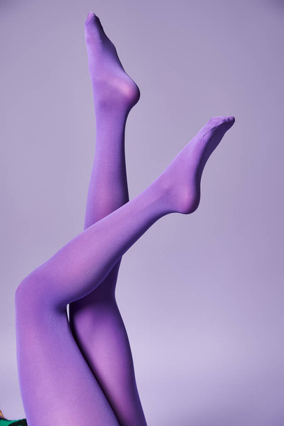 Μια νεαρή γυναίκα δείχνει τα πόδια της με ζωντανές κάλτσες σε ένα μωβ φόντο σε ένα στούντιο. - Φωτογραφία, εικόνα
