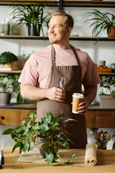 Un uomo in grembiule che tiene una tazza di caffè in un negozio di piante. - Foto, immagini