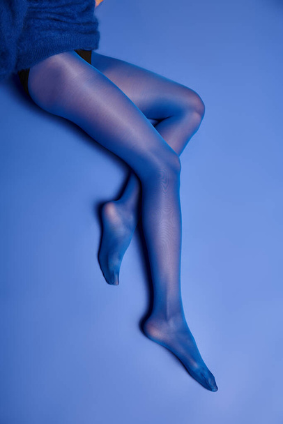 Μια νεαρή γυναίκα δείχνει τα πόδια της σε ζωντανές μπλε κάλτσες, ενώ χτυπά μια στάση σε ένα σκηνικό σε ένα στούντιο. - Φωτογραφία, εικόνα