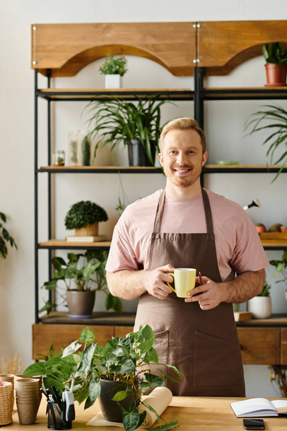 Un hombre con estilo en un delantal disfrutando de una taza de café en una tienda de plantas, encarnando el propio concepto de negocio. - Foto, Imagen