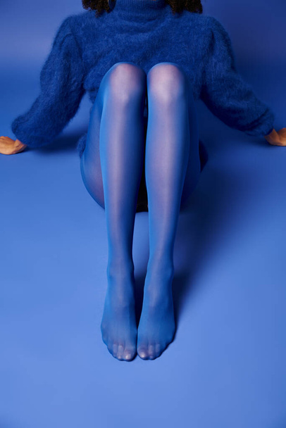 Μια νεαρή γυναίκα με ένα εντυπωσιακό μπλε φόρεμα ποζάρει ενώ κάθεται στο έδαφος με έναν αέρα γαλήνης και κομψότητας. - Φωτογραφία, εικόνα