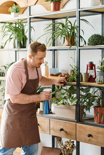 Мужчина стоит перед полкой, заполненной различными растениями в маленьком заводском магазине, демонстрируя любовь к природе и страсть к своему бизнесу.. - Фото, изображение