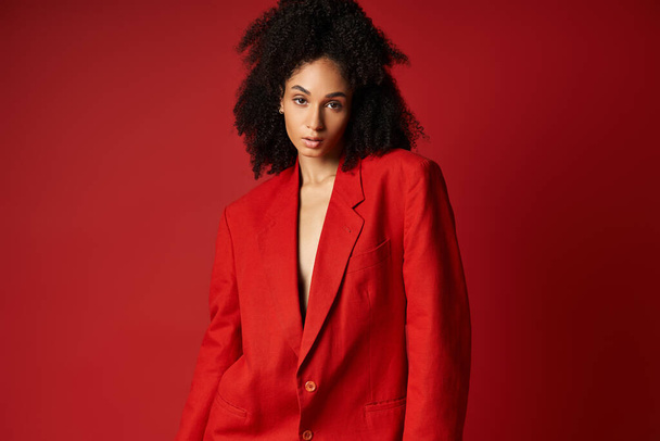 Eine junge Frau strahlt Zuversicht in einem lebendigen Atelier aus und trägt einen auffallend roten Anzug, als sie für ein Foto posiert. - Foto, Bild