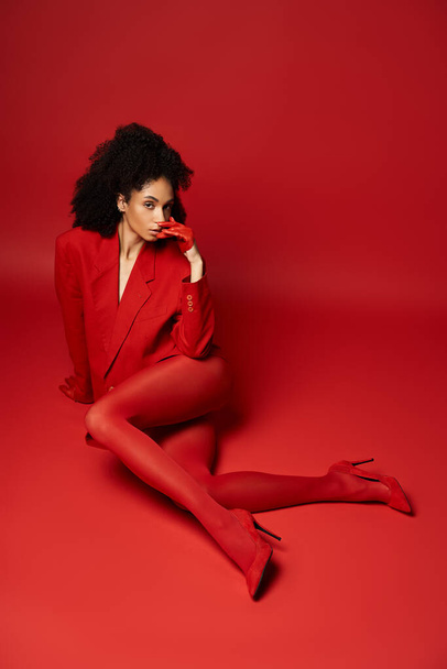 Nuori nainen silmiinpistävässä punaisessa puvussa istuu sulavasti vilkkaalla taustalla studioympäristössä.. - Valokuva, kuva