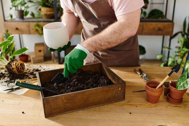 Un hombre en un delantal y guantes planta varias plantas en una caja en una tienda de plantas, encarnando la esencia de un dueño de una pequeña empresa. - Foto, imagen