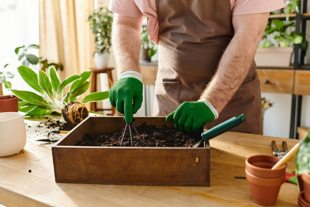 Um homem de luvas verdes transfere cuidadosamente o solo para uma caixa em uma loja de plantas, mostrando sua paixão por seu próprio pequeno negócio.. - Foto, Imagem