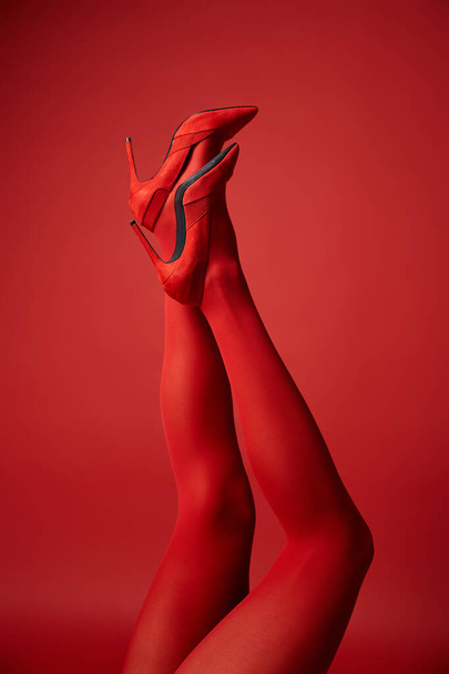 Eine junge Frau präsentiert ihre Beine in Strumpfhosen vor einem kräftigen roten Hintergrund und strahlt Stärke und Zuversicht aus. - Foto, Bild