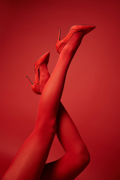 Eine junge Frau in roten Strümpfen und High Heels, die ihre Beine in einer verführerischen Pose vor einem lebendigen Studiohintergrund zur Schau stellt. - Foto, Bild