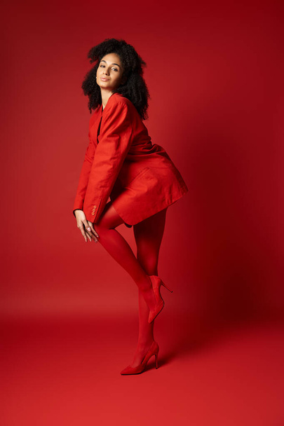 Egy fiatal nő eleganciát áraszt feltűnő piros ruhában, pózol a kamerának élénk stúdió háttér mellett.. - Fotó, kép