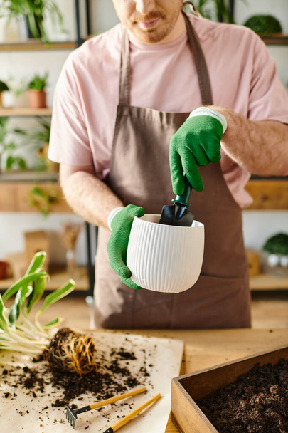 Mężczyzna w fartuchu i zielonych rękawiczkach pilnie podlewa rośliny w otoczeniu botanicznym. - Zdjęcie, obraz