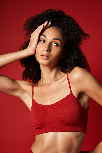 Levendige jonge vrouw poseert vol vertrouwen in een opvallende rode sportbeha voor een stijlvolle fotoshoot. Studio-instelling. - Foto, afbeelding
