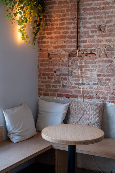 Het beeld toont een gastvrije hoek in een modern café, een combinatie van rustieke charme en eigentijds design. Een ronde houten tafel staat op de voorgrond en nodigt uit tot een moment van ontspanning of gesprek - Foto, afbeelding