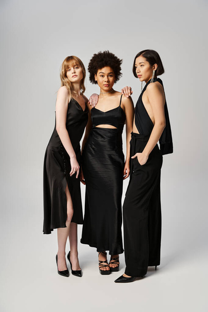 Tre donne di sfondi diversi in piedi insieme elegantemente su uno sfondo grigio studio. - Foto, immagini