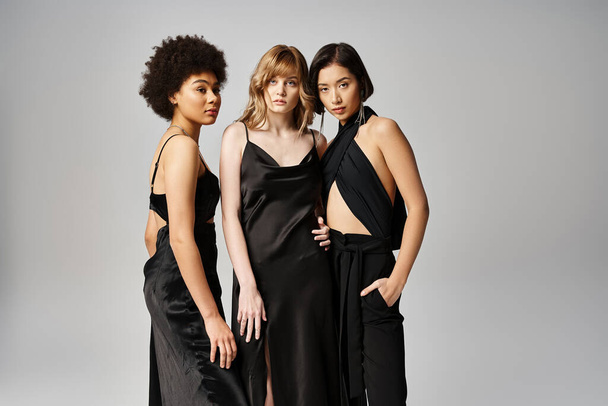 A group of three beautiful women of Caucasian, Asian, and African American descent standing gracefully together against a grey studio backdrop. - Photo, Image