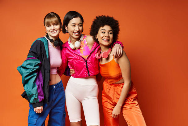 Drei schöne Frauen, die Vielfalt und Einheit repräsentieren, stehen zusammen vor orangefarbenem Hintergrund. - Foto, Bild