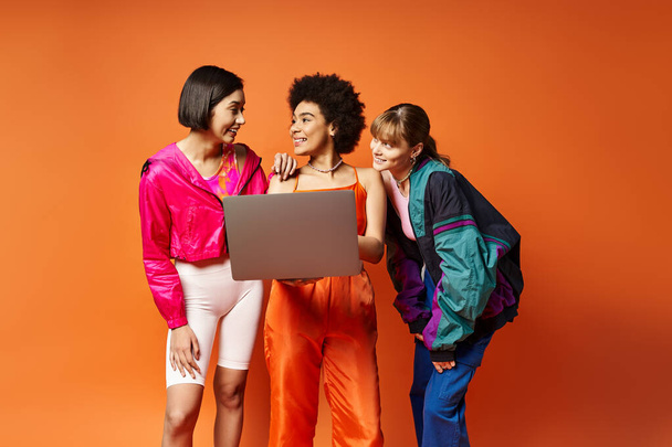 Tre donne - caucasica, asiatica, afroamericana - stanno insieme su uno sfondo arancione studio, irradiando bellezza e diversità. - Foto, immagini