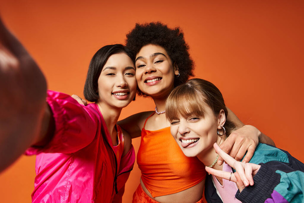 Een groep verschillende vrouwen legt momenten vast met een mobiele telefoon tegen een oranje studio achtergrond. - Foto, afbeelding