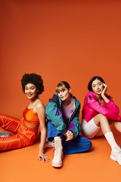 Un groupe diversifié de jeunes femmes assises ensemble, mettant en valeur la beauté multiculturelle sur un fond orange. - Photo, image