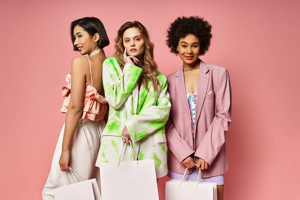 Tres mujeres de diferentes etnias sosteniendo bolsas de compras contra un fondo de estudio rosa. - Foto, Imagen