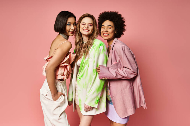 Τρεις γυναίκες διαφορετικών εθνικοτήτων στέκονται μαζί, επιδεικνύοντας πολυπολιτισμική ομορφιά σε ένα ροζ φόντο στούντιο. - Φωτογραφία, εικόνα
