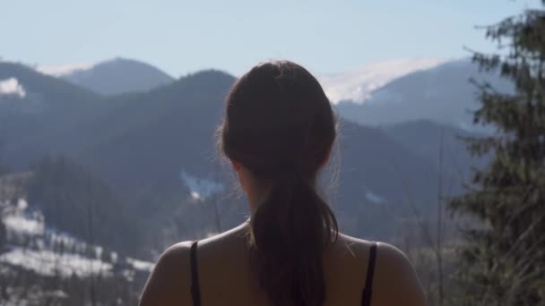 A lány a kamerába mosolyog, és elfordul, hogy megfigyelje a nyugodt hegyvonulatot tavasszal. - Felvétel, videó