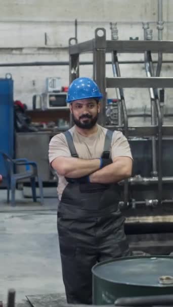 Vertikální stopovací portrét sebevědomého pracovníka z Blízkého východu v kombinéze a tvrdé čepici s rukama složenýma na pracovišti - Záběry, video