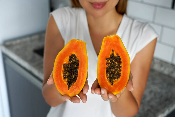Giovane donna non identificata che mostra una papaia tagliata in due metà in cucina - Foto, immagini