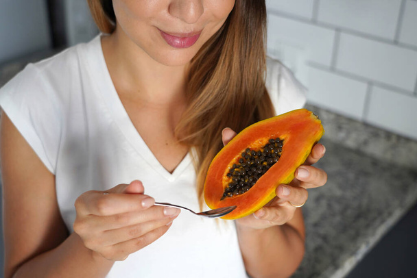 Mujer joven no identificada sosteniendo media fruta de papaya y cuchara en la cocina - Foto, imagen
