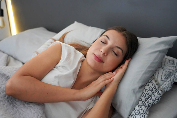 Σημασία ενός καλού ύπνου. Νεαρή όμορφη γυναίκα κοιμάται μακάρια στο κρεβάτι. Κορίτσι με ρυθμιζόμενο κύκλο τσίρκου. - Φωτογραφία, εικόνα