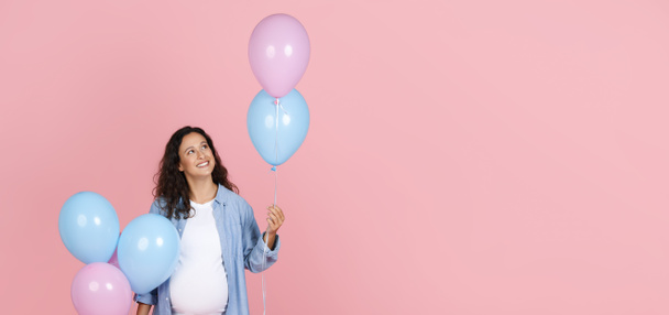 Positiv schöne junge werdende Frau mit dickem Bauch, die rosa und blaue Luftballons in der Hand hält, Geschlecht verraten Party-Feier, isoliert auf rosa Hintergrund, Panorama mit Kopierraum - Foto, Bild
