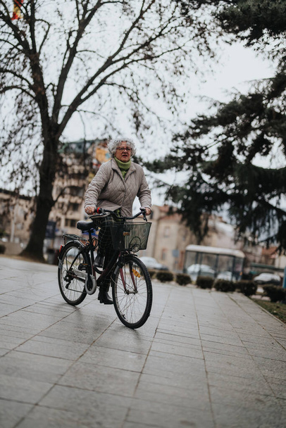 Uma pessoa idosa gosta de andar de bicicleta em um caminho pavimentado em um parque da cidade durante o outono, mostrando um estilo de vida ativo. - Foto, Imagem