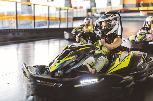 Jonge vrouw in helm en race handschoenen concurreren in een indoor go-kart race. - Foto, afbeelding
