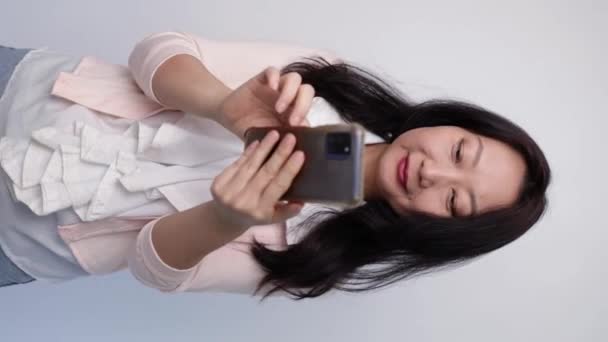 垂直ビデオ, ハッピーアジアのビジネス女性 手の携帯電話で良いニュースを得る, スタジオの白い背景に孤立. - 映像、動画