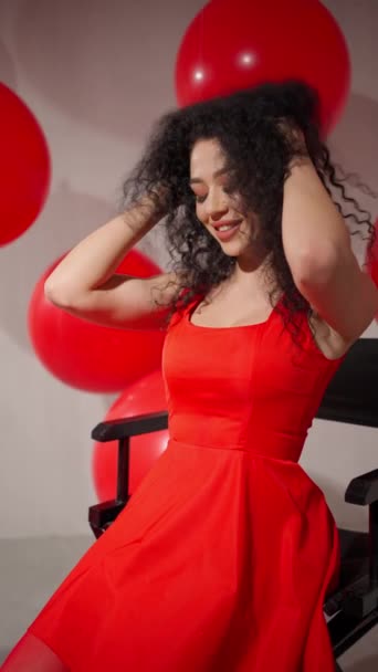 Radiante Schumann en vestido rojo se sienta felizmente lanzando su pelo y mirando entre globos rojos - Metraje, vídeo