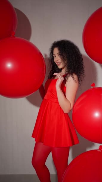 Γυναίκα με κόκκινο φόρεμα και καλσόν με σγουρά μαλλιά, ποζάρει με μεγάλα μπαλόνια. - Πλάνα, βίντεο