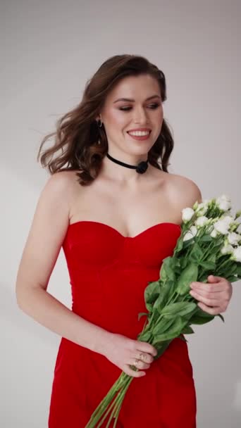 Ein strahlendes Lächeln ergänzt ihr schulterfreies rotes Kleid, während sie einen frischen weißen Strauß greift und der Szene einen Hauch natürlicher Eleganz verleiht.. - Filmmaterial, Video