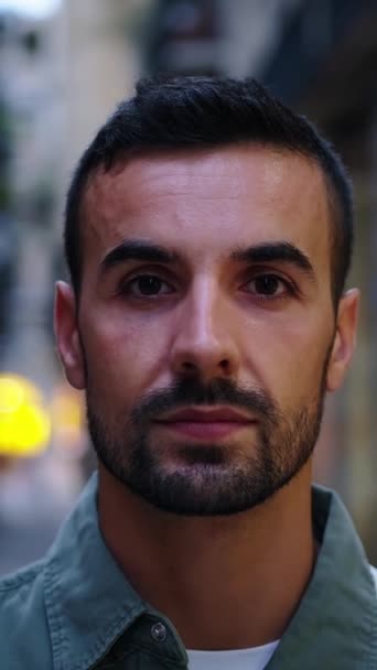 Vertical camera zooming face young bearded handsome man stands looking serious at camera on street in European city Barcelona. Confident Caucasian male tourist posing earnest of outdoor night tourism - Video, Çekim