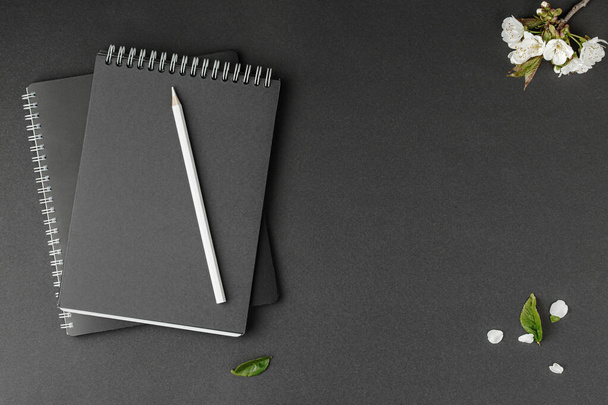 Zwart notitieboekje met witte spiraal, potlood en witte bloemen op geïsoleerde achtergrond. Wit en zwart concept. - Foto, afbeelding