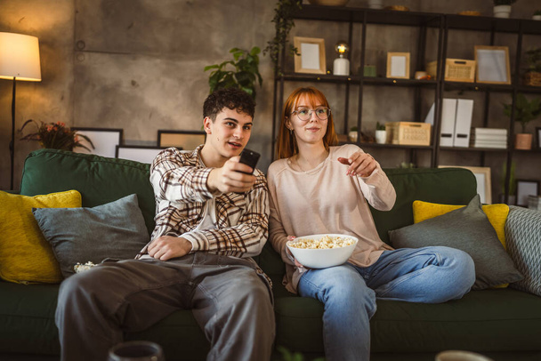 Pár kaukázusi férfi és nő ül otthon kanapén TV-t néz - Fotó, kép