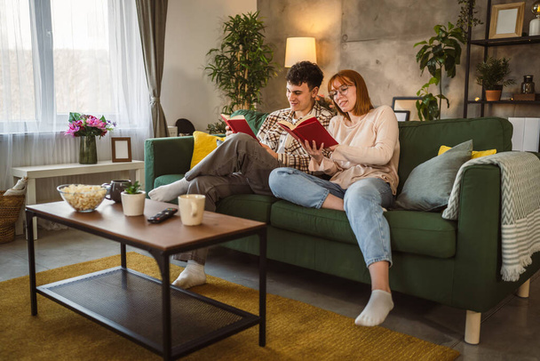 Erkek ve kadın Kafkasyalı yetişkin çift evde kanepe yatağında kitap okuyor. - Fotoğraf, Görsel